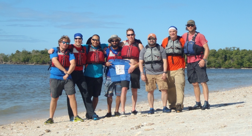 a group of people stand on a beach smiling while posing with a blue peter flag